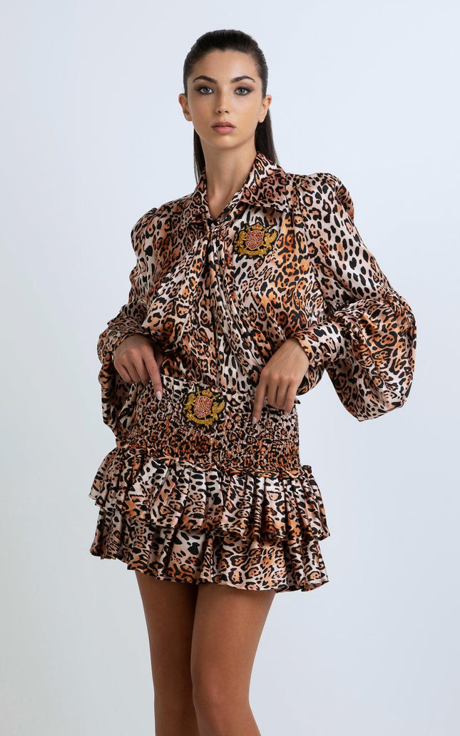 Woman wearing a leopard print mini dress with ruffled skirt and gold crest patches