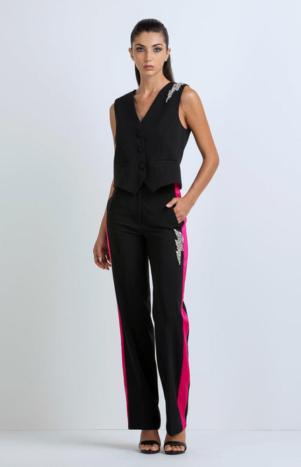 Woman wearing a black sleeveless vest and black pants with magenta side stripes and silver embellishments