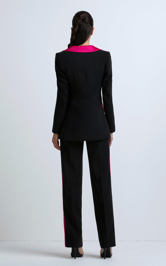 Woman wearing black tailored pantsuit with pink collar and side stripes, back view