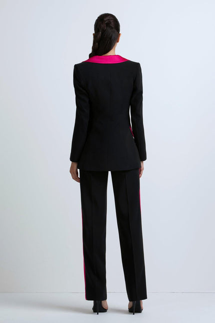 Woman wearing black tailored suit with pink collar and pink side stripes, back view