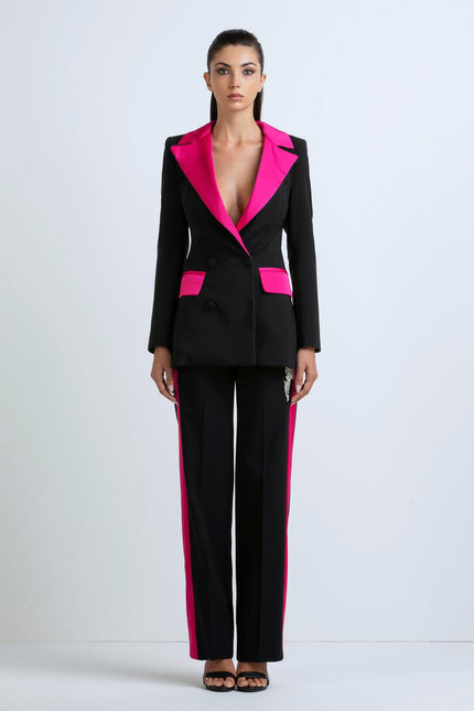 Woman wearing a black suit with hot pink lapels and side stripes, standing against a plain background