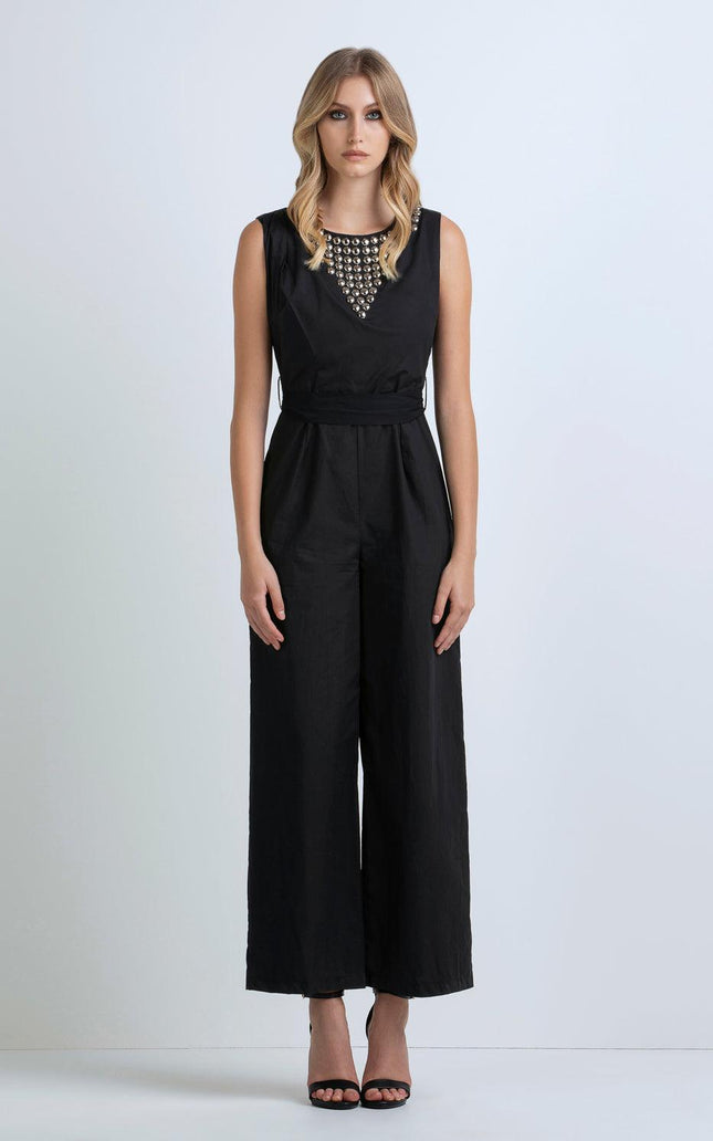 Woman wearing a sleeveless black jumpsuit with metallic studded neckline and wide legs