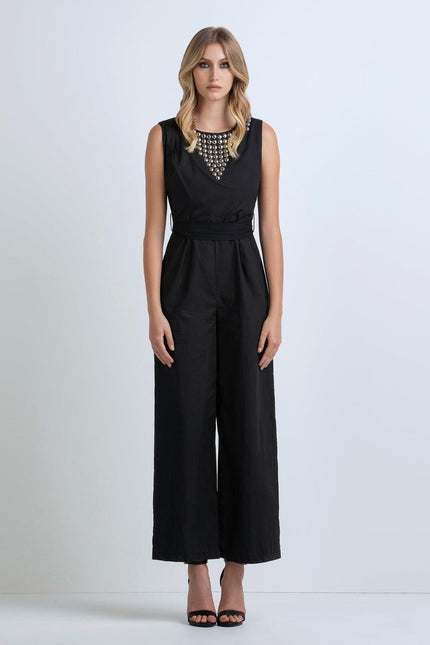 Woman wearing a sleeveless black jumpsuit with metallic studded neckline and wide legs