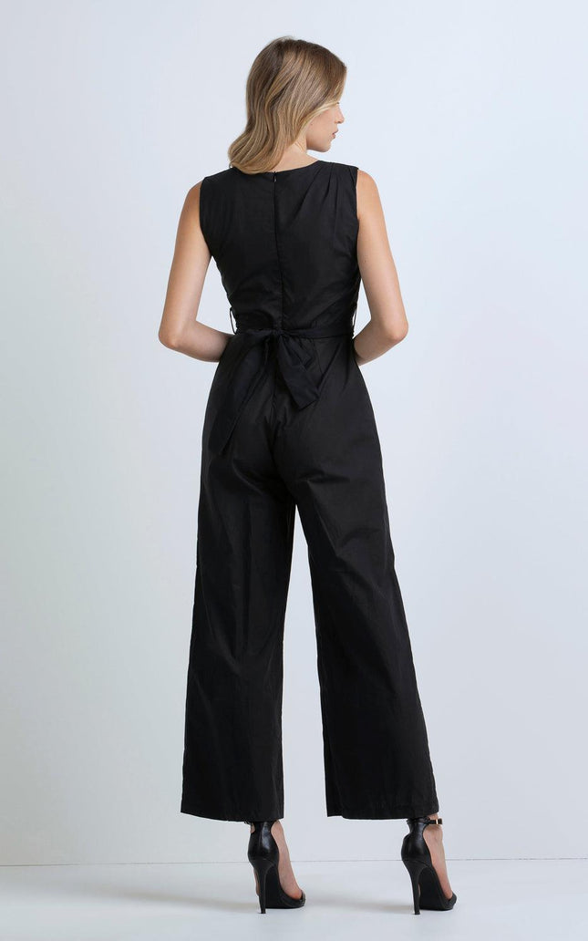 Woman in sleeveless black jumpsuit with tied waist and wide legs, back view