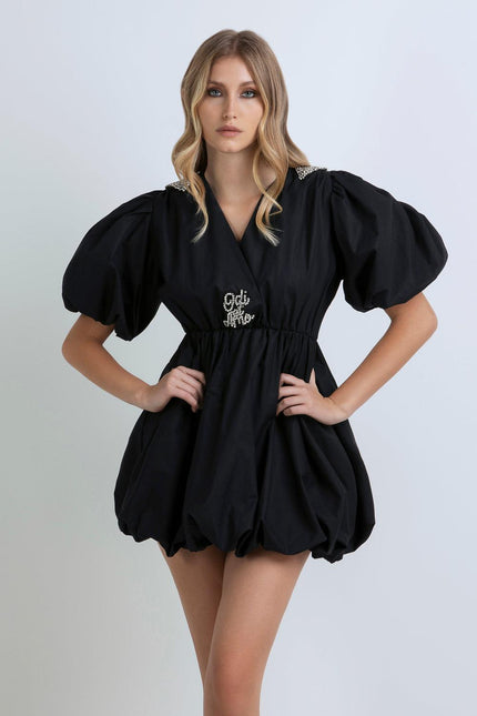 Woman wearing a black puff sleeve mini dress with pearl details and Odi et Amo embroidery