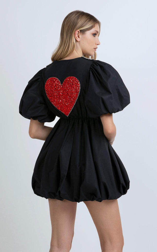 Woman in black puff sleeve mini dress with large red sequin heart on the back