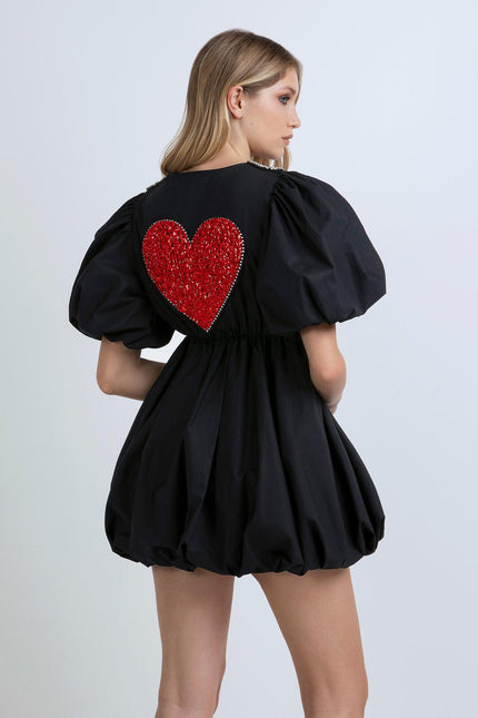 Woman in black puff sleeve mini dress with large red sequin heart on the back