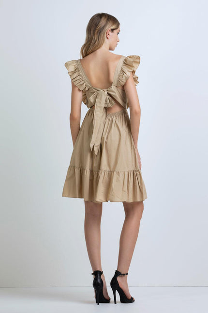 Woman wearing beige ruffle sleeve dress with open back and bow detail, high heels