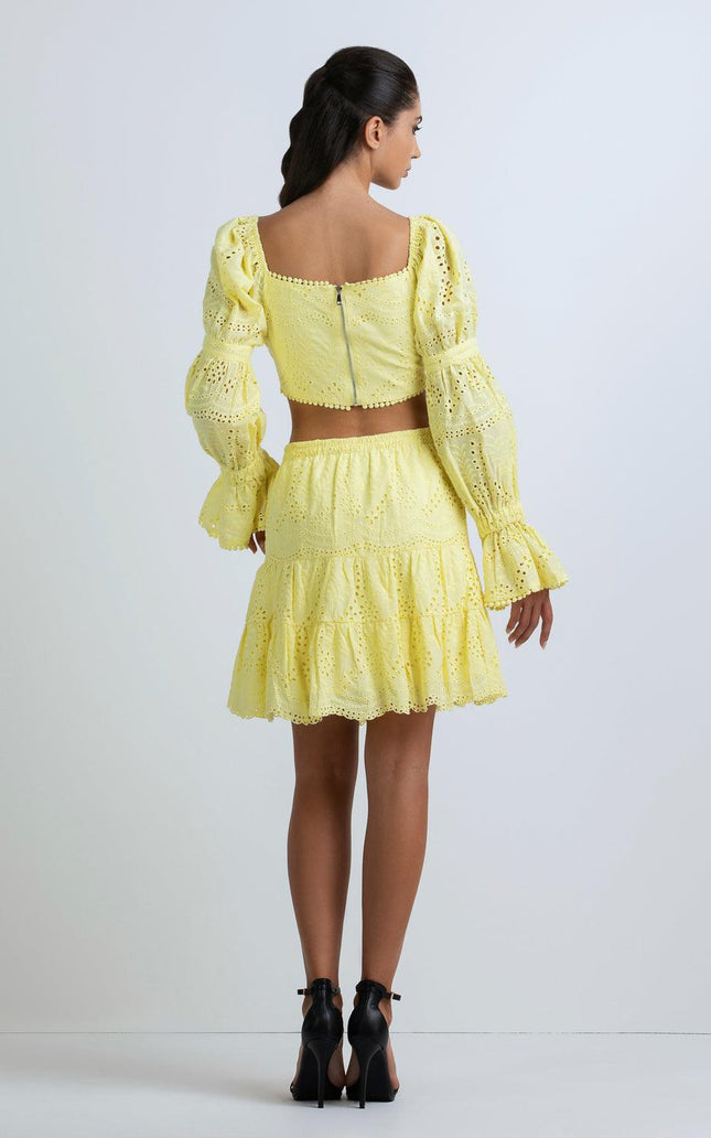 Woman in yellow eyelet skirt and ruffled crop top with puff sleeves, back view