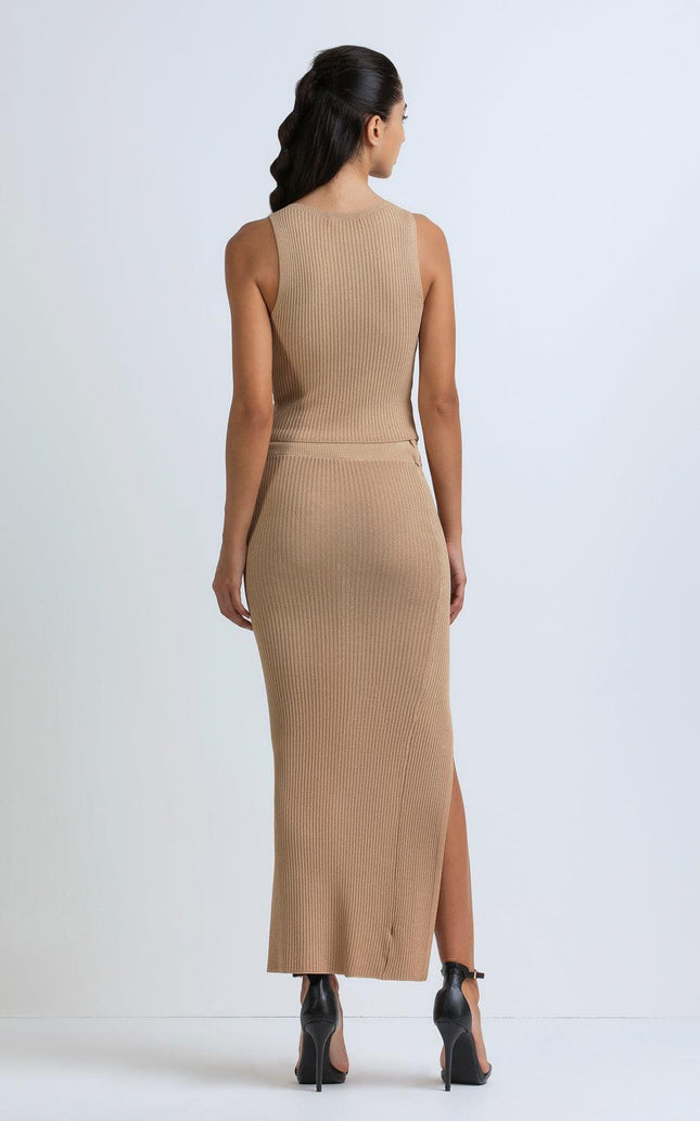 Woman wearing sleeveless ribbed beige knit dress with side slit and black heels, back view