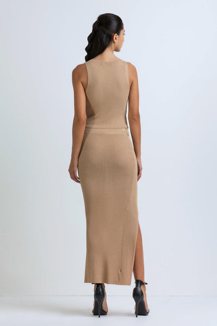 Woman wearing sleeveless ribbed beige knit dress with side slit and black heels, back view