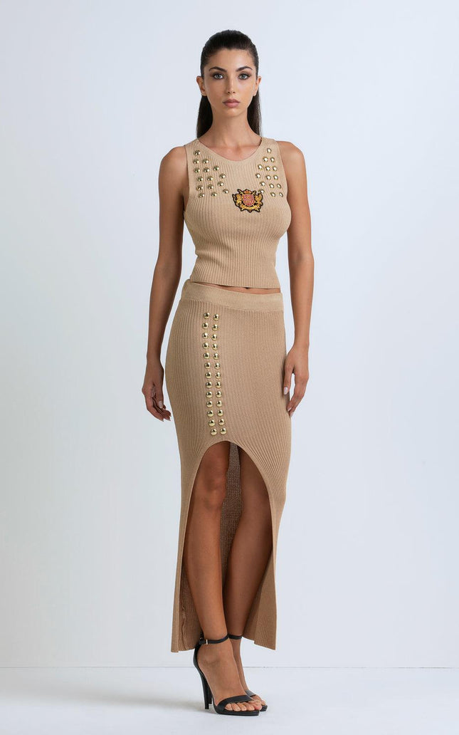 Woman wearing ribbed beige knit crop top and matching midi skirt with gold studs and front slit