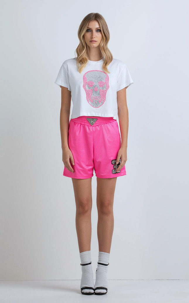 Woman wearing a white crop top with pink skull graphic and bright pink high-waisted shorts