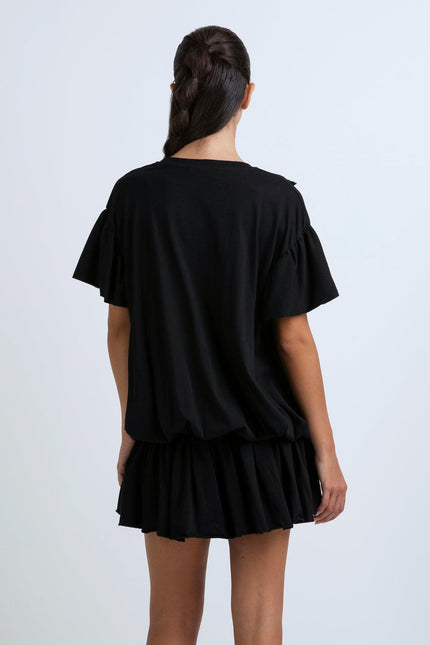 Woman in black short dress with ruffle sleeves and pleated skirt, back view