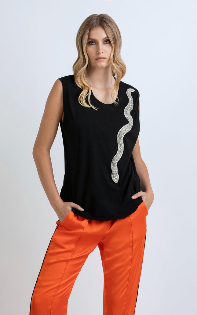 Woman in black sleeveless top with sequin snake detail and orange satin pants