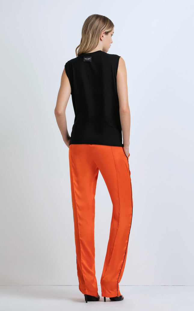 Woman in sleeveless black top and bright orange pants, standing against white background