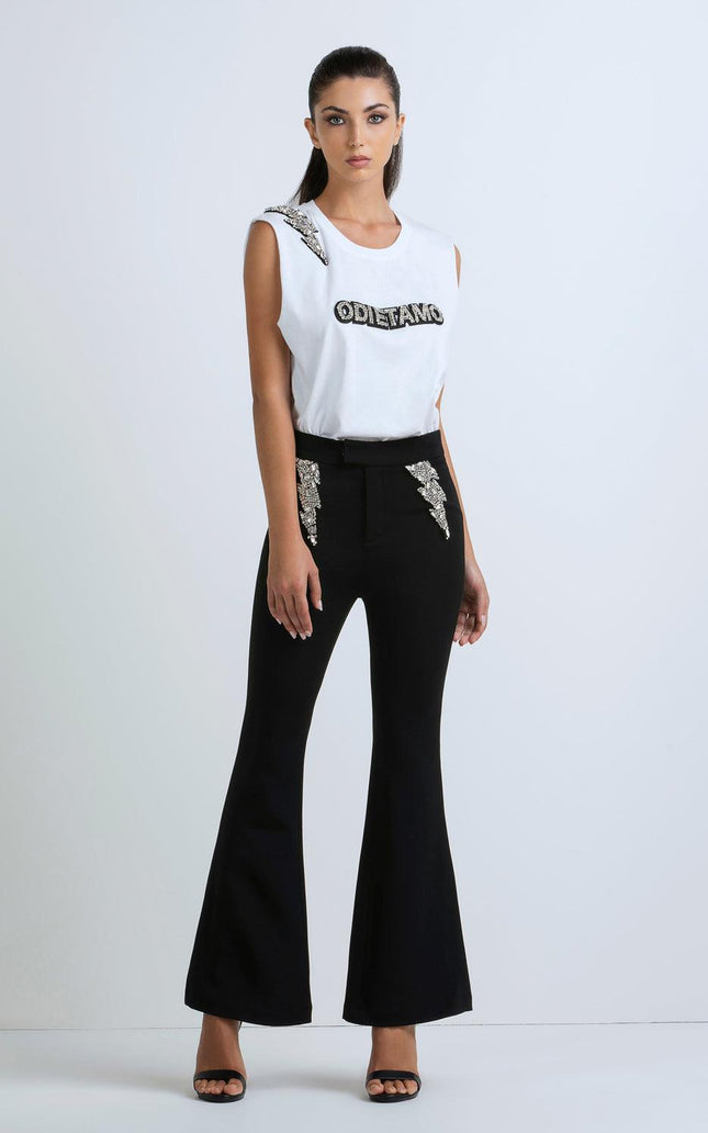 Woman in a sleeveless white top with bold text and flared black pants with sequin accents