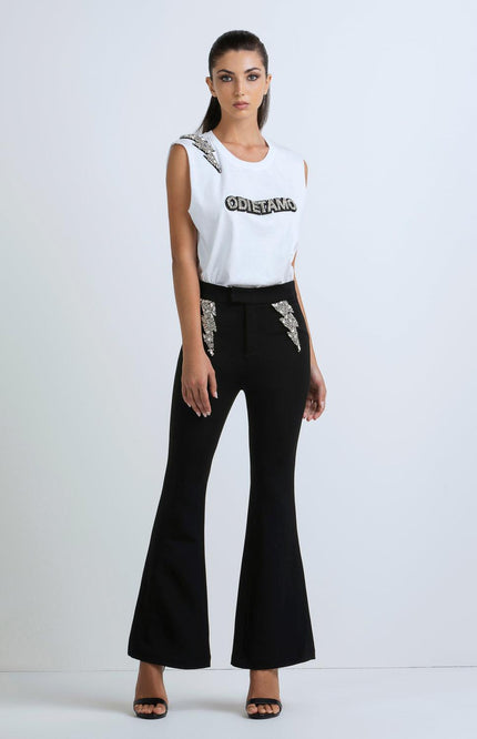 Woman in a sleeveless white top with bold text and flared black pants with sequin accents
