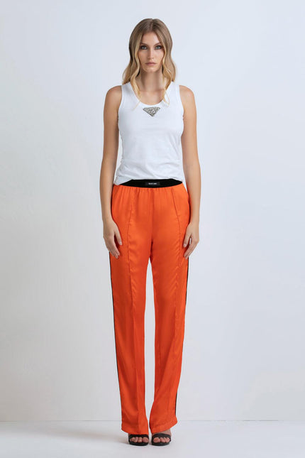 Woman wearing white tank top with jewel detail and vibrant orange satin pants