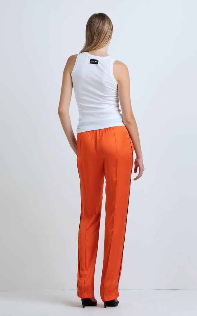 Woman in white tank top and orange satin pants, back view, standing indoors