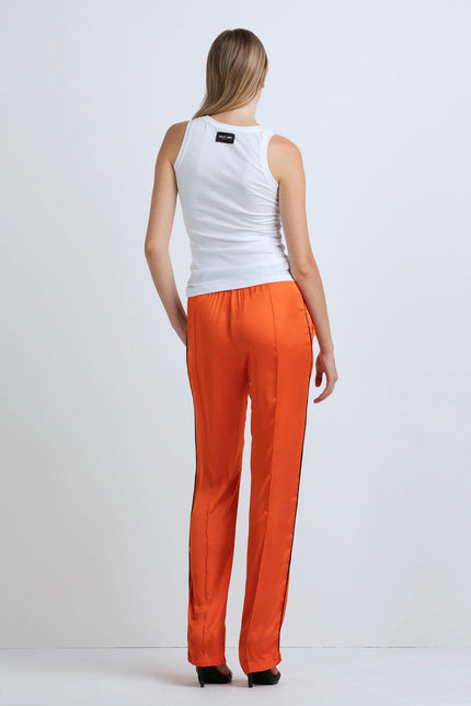 Woman in white tank top and orange satin pants, back view, standing indoors