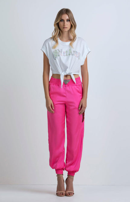 Woman wearing a white knotted crop top and bright pink jogger pants, fashion outfit