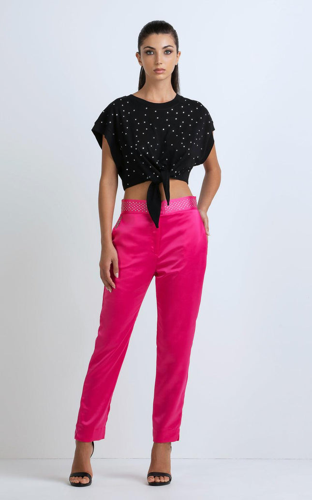 Woman in black studded crop top and bright pink pants, stylish modern fashion outfit