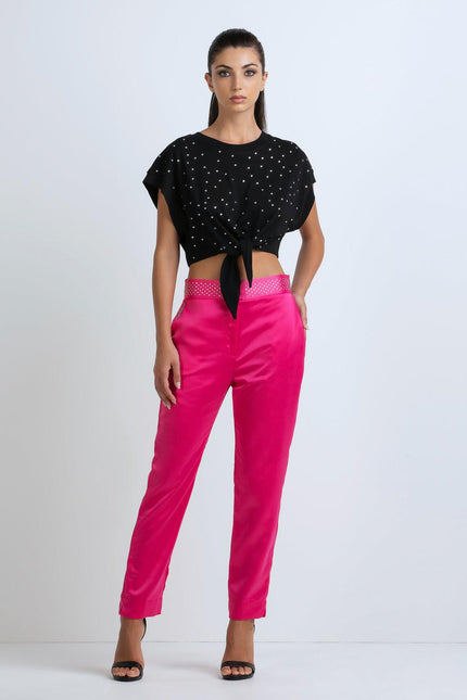 Woman in black studded crop top and bright pink pants, stylish modern fashion outfit