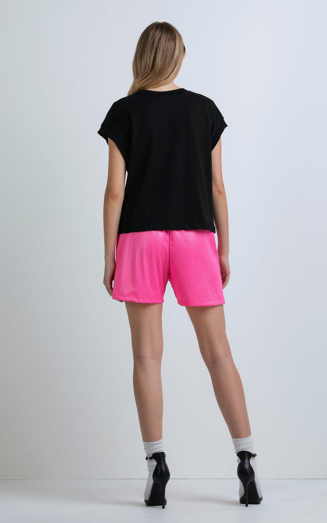 Woman in black t-shirt and bright pink shorts, white socks, black heels, studio backdrop
