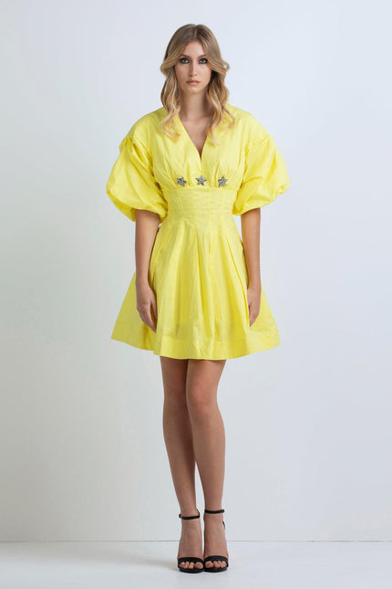 Woman wearing a short yellow dress with puff sleeves and star embellishments, fashion studio shot