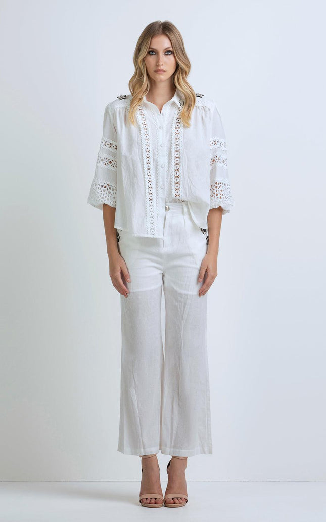 Woman wearing a white lace blouse with wide sleeves and white wide-leg pants