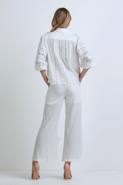 Back view of woman in white lace blouse with wide sleeves and white flared pants