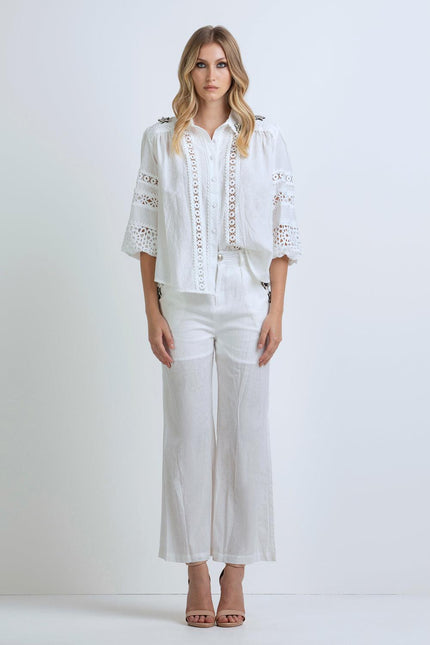 Woman wearing white lace-detailed blouse and wide-leg trousers, standing in studio