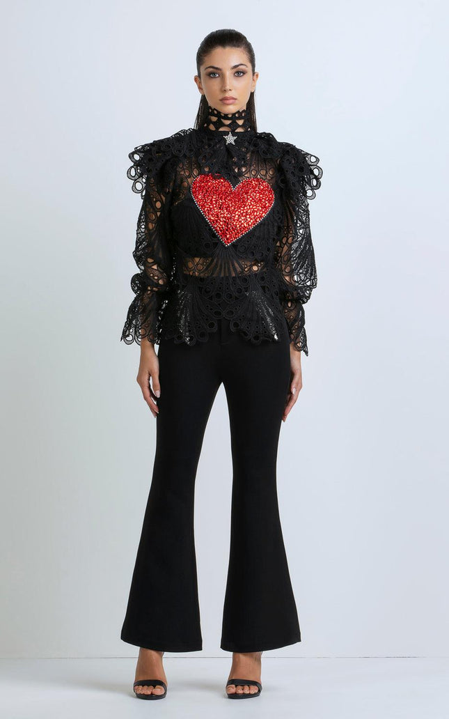 Woman wearing black lace top with red heart detail and flared black pants, standing indoors