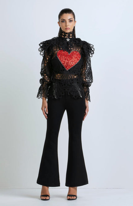 Woman wearing black lace top with red heart detail and flared black pants, standing indoors