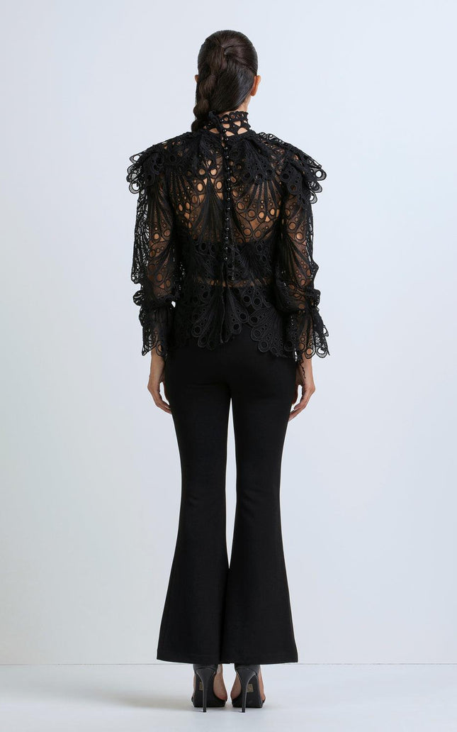 Woman in black lace blouse with ruffle details and flared black pants, rear view