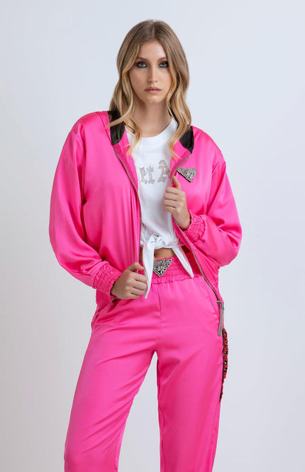 Woman wearing a vibrant pink satin tracksuit with rhinestone details and a white knotted T-shirt