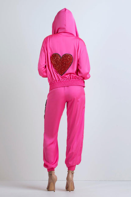 Woman in pink tracksuit with sequin red heart on back and hood, standing indoors