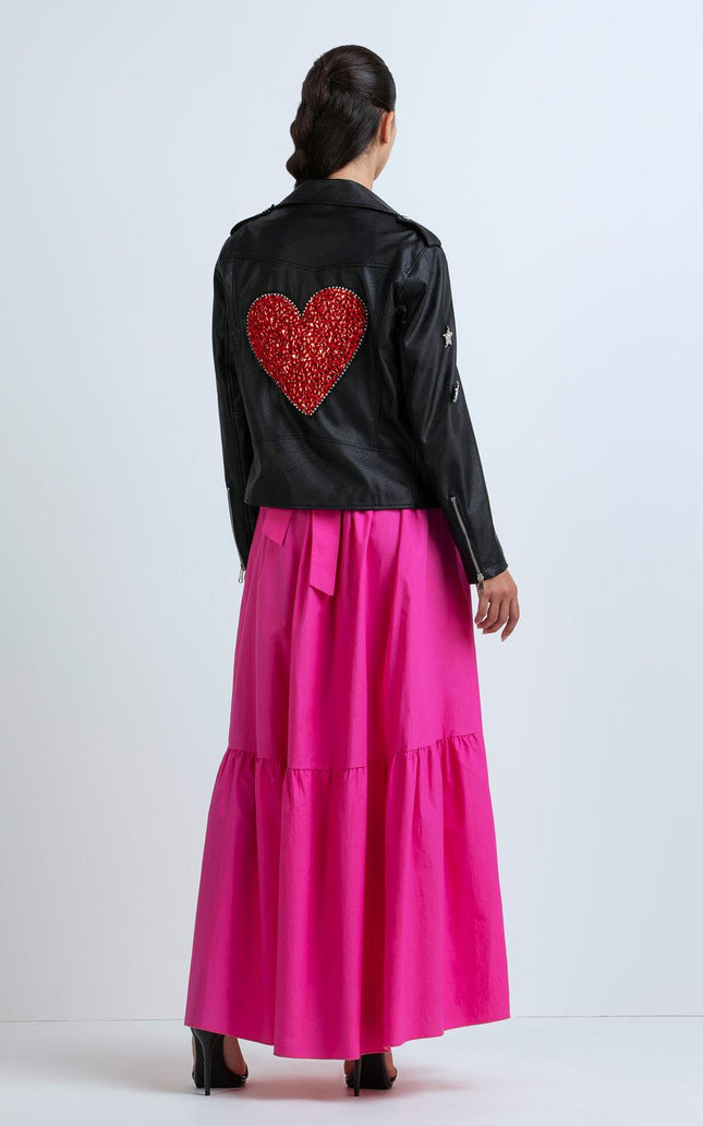 Woman wearing black leather jacket with red heart patch and vibrant pink maxi skirt