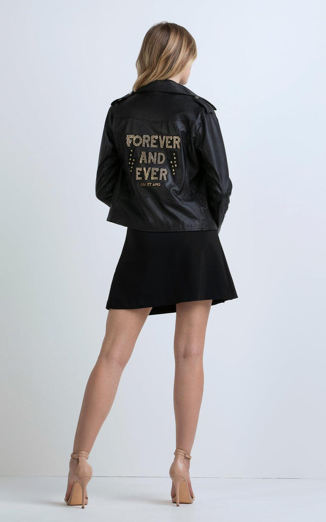 Woman in black faux leather jacket with 'Forever and Ever' gold studded detail, black skirt, nude heels