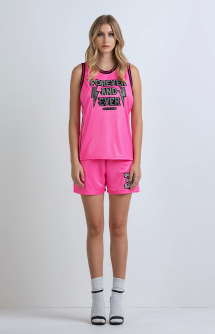 Woman wearing bright pink mesh tank top and shorts set with sporty chic style, text print, and socks with heels.
