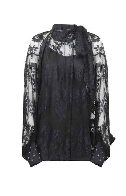Camicia da sera in pizzo nero effetto mesh trasparente con polsini gioiello scintillanti, abbinata a pantaloni sartoriali color ruggine.