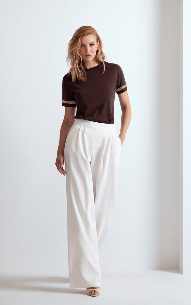 Donna con t-shirt marrone con dettagli strass sulle maniche e pantaloni larghi bianchi.