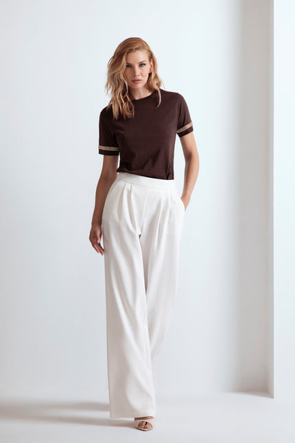 Donna con t-shirt marrone con dettagli strass sulle maniche e pantaloni larghi bianchi.