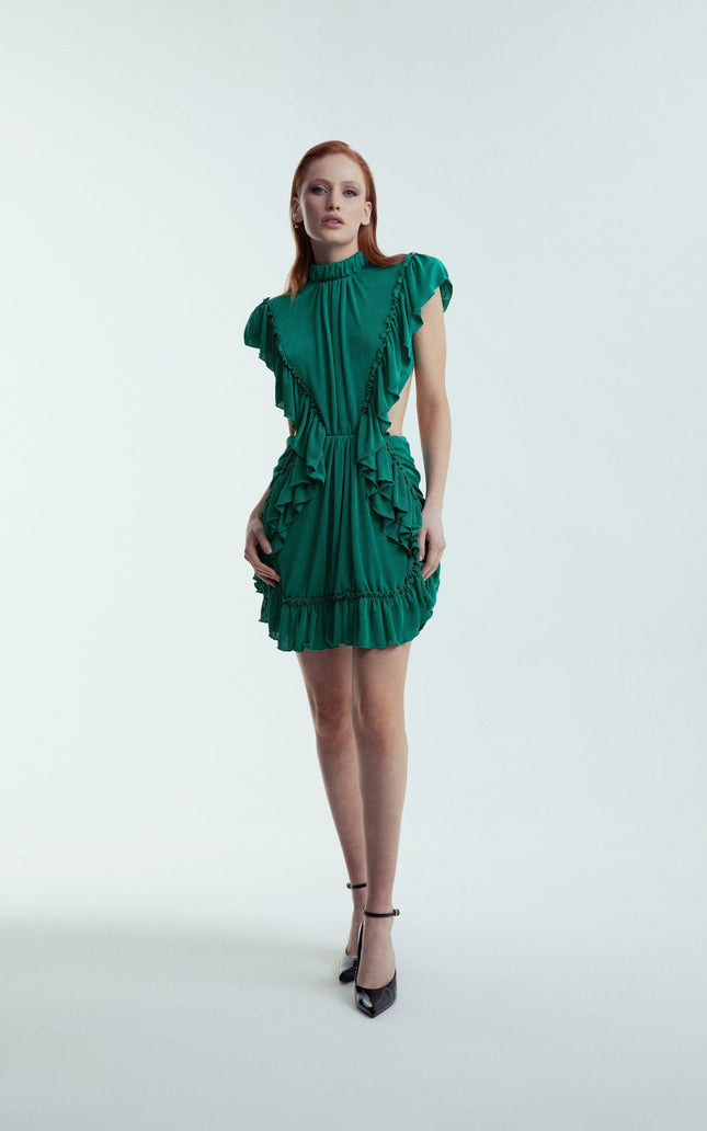 Woman wearing a green ruffled mini dress with high neckline and black heels, studio background