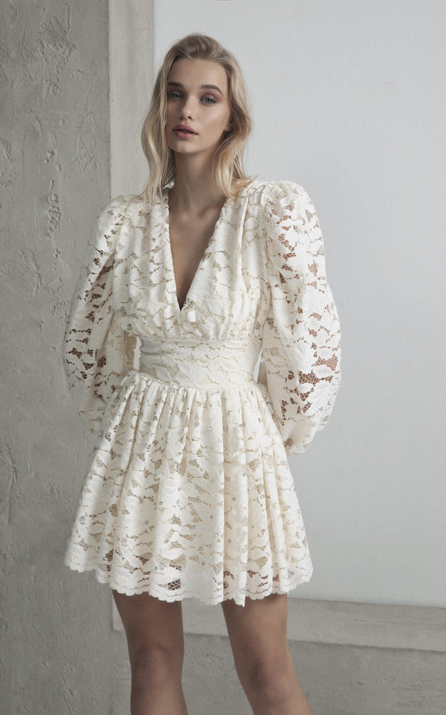 Woman wearing a white lace mini dress with puff sleeves and deep V-neck