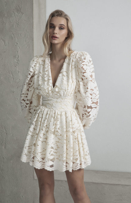 Woman wearing a white lace mini dress with puff sleeves and deep V-neck
