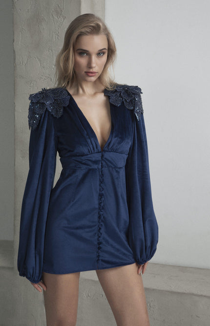 Woman in deep blue mini dress with long sleeves and embellished floral shoulders