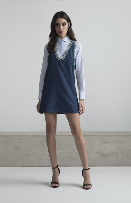 Woman in denim mini dress with crystal straps over white shirt, fashion-forward outfit
