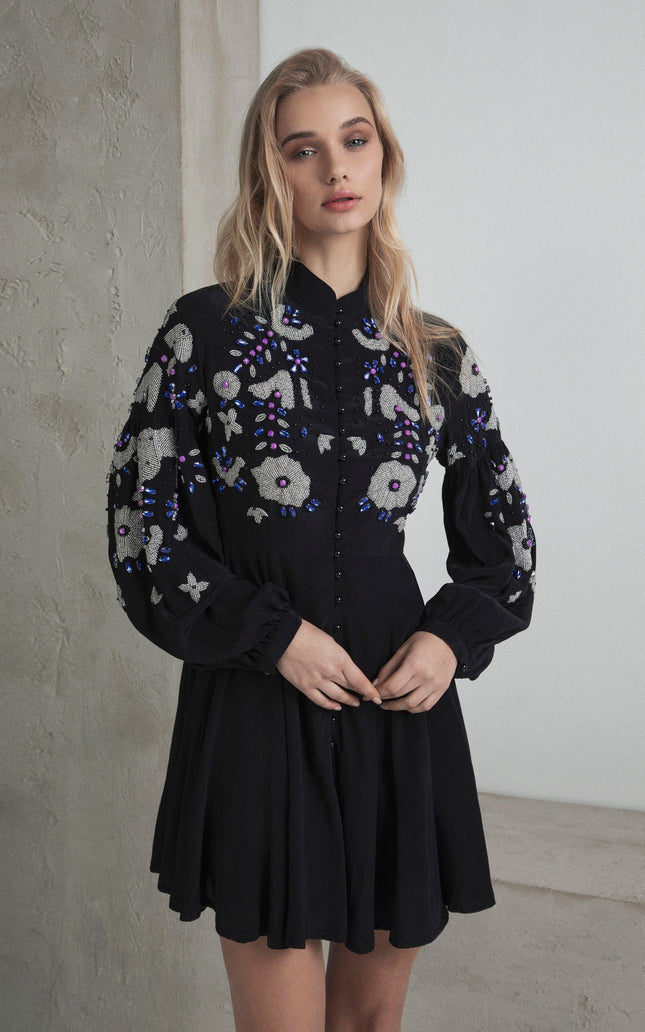 Woman wearing a black mini dress with floral embroidery and long sleeves